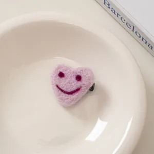 Nahaufnahme einer Haarspange aus rosa Filzherz mit besticktem Lächeln auf einem Teller