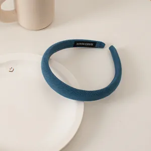 Detail of blue ribbed fabric headband with handmade label on white ceramic plate