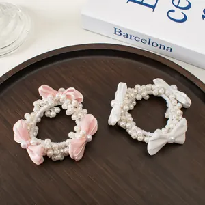 Détail de chouchous en perles avec nœuds en satin rose et blanc sur plateau bois