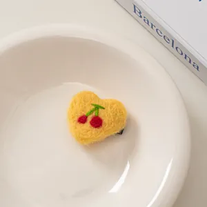 Nahaufnahme einer Haarspange aus gelbem Wollfilz in Herzform mit Kirsch-Stickerei