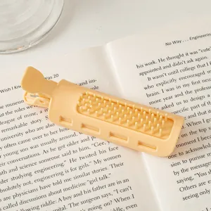 Close-up of a pale yellow plastic hair root clip with teeth on an open book