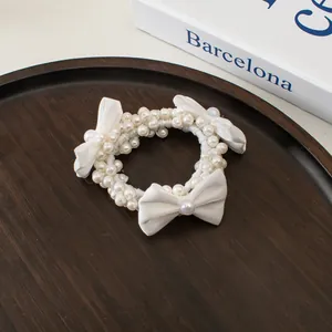 Détail d'un chouchou en perles blanches avec nœuds en soie sur plateau en bois