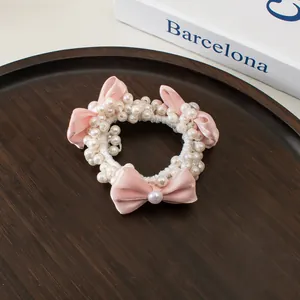 Détail de l'élastique à perles avec nœuds en satin rose sur un fond en bois texturé