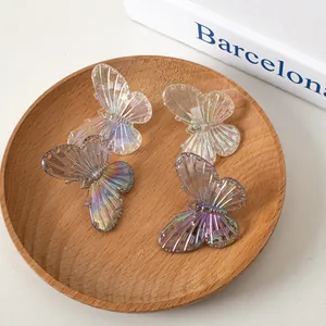 Dettaglio di quattro fermagli a farfalla iridescenti color pastello su vassoio di legno