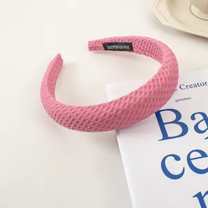 Détail d'un serre-tête rose en tissu gaufré avec étiquette faite main sur décor blanc chic