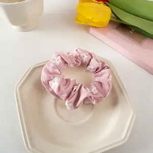 Close-up of pink fabric scrunchie with white daisy floral print on a ceramic tray