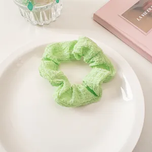 Close-up of light green seersucker scrunchie on a white ceramic plate with soft shadows