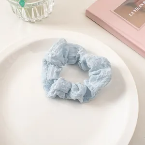 Close-up of light blue seersucker hair scrunchie with pleated texture on white ceramic tray