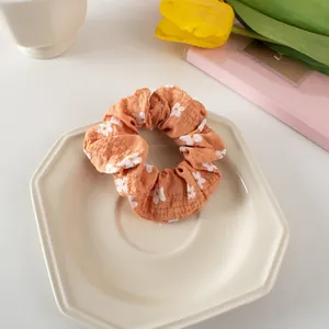 Detail of warm orange scrunchie with white daisy floral patterns on soft fabric