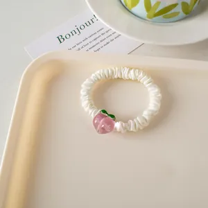 Primer plano de un coletero de satén blanco crema con un lindo colgante de melocotón rosa