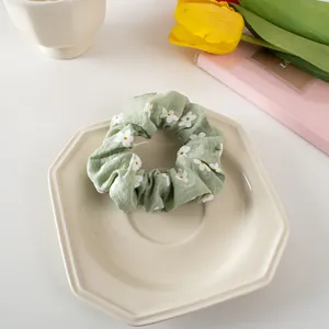 Detailed close-up of a light green floral scrunchie with white daisy prints on a ceramic plate