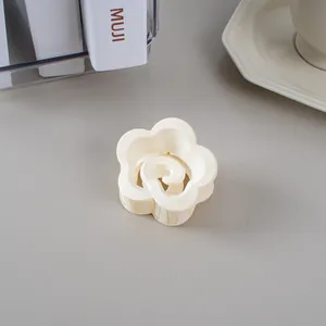 Vue détaillée d'une pince à cheveux mate en forme de fleur crème sur fond gris épuré