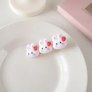 Détail de trois lapins 3D blancs avec des fraises sur une pince à cheveux dorée