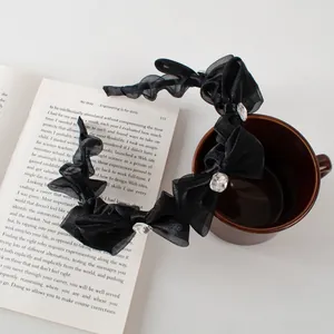 Elegant black mesh bow headband with square rhinestones shown on a white book and coffee cup