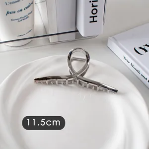 Détail d'une pince à cheveux argentée de 11,5 cm au design ajouré croisé sur plat blanc