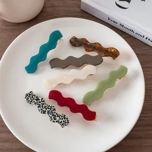 Set of seven colorful wavy acetate hair clips with golden metal springs on a white plate