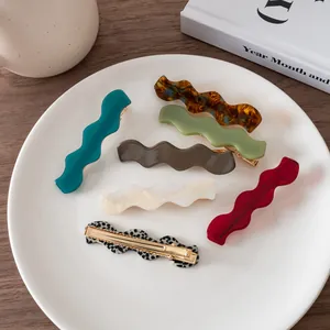 Close-up of wavy acetate hair clips in assorted colors arranged on a white ceramic plate