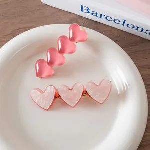 Pink heart-shaped acetate hair clips set in a white ceramic dish on a wooden table