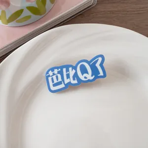 Détail d'une pince à cheveux en acrylique bleu avec texte Barbie Q blanc sur plat