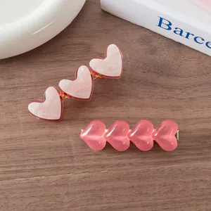 Close-up of pink heart-shaped acetate hair clips with marble texture on dark wood