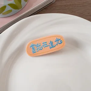 Détail d'une pince à cheveux orange avec broderie bleue et texte chinois sur plat