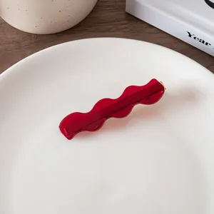 Close-up of a wavy burgundy acetate hair clip with golden metal clip on a ceramic plate