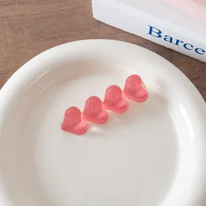 Detail of four pink jelly heart charms on a gold hair clip placed on a white ceramic plate