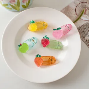 Detail of five colorful fruit hair clips with glitter texture on a white ceramic plate