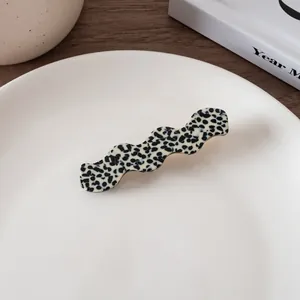 Detail of wavy acetate hair clip with black and white spotted pattern on a ceramic plate