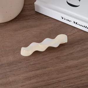Close-up of wavy acetate hair clip in pearl white finish on a minimalist background