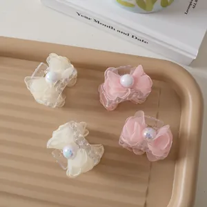 Detail of four small mesh bow hair clips with white faux pearls on a beige tray