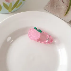 Detail of pink peach resin hair clip with frosted texture and green leaves on white plate