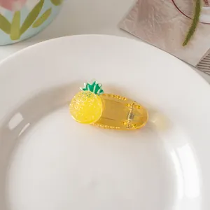 Detail of yellow pineapple hair clip with green leaves on white plate in soft lighting