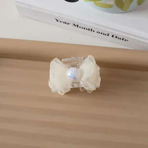 Close-up of small mesh bow hair clip with iridescent faux pearl on a cream background