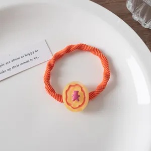Detail eines orangefarbenen Haargummis mit gelbem Harz-Oval und lila Bären-Charm