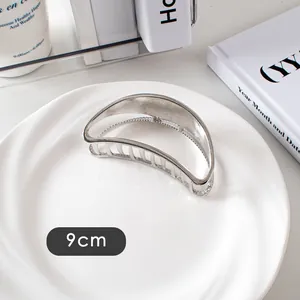 Détail d'une pince à cheveux argentée de 9cm avec un design en croissant évidé