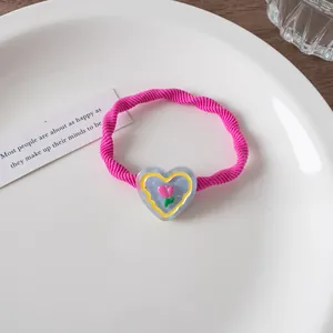 Nahaufnahme eines rosa Haargummis mit Tulpen-Herz-Anhänger aus Harz auf weißem Porzellan