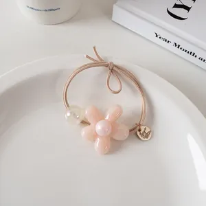 Détail d'élastique à cheveux fleur pastel avec pétales en résine et perles sur plat blanc