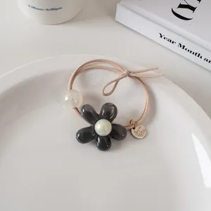 Détail d'un élastique à cheveux fleur fait main avec pétale gelée et perle sur plat en céramique