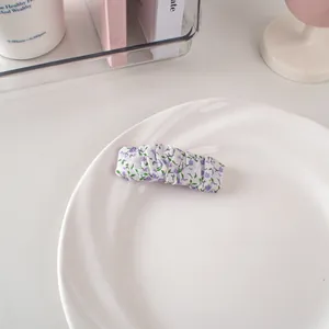 Dettaglio di un fermaglio per capelli in tessuto a fiori viola su sfondo bianco