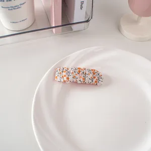 Dettaglio del fermaglio per capelli in tessuto a fiori arancioni su un piatto bianco