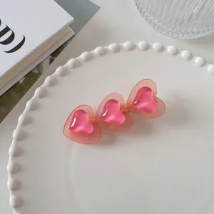 Détail d'une pince à cheveux rose triple cœur en résine mate avec une base en métal doré