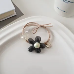 Détail d'un élastique à cheveux fleur avec perle nacrée et petit pendentif doré