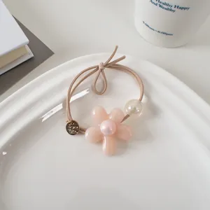 Détail d'un élastique à fleurs roses avec perle et bille irisée dans une assiette en céramique