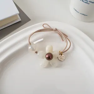 Détail d'un élastique à cheveux fleur perle blanche posé sur un plateau en céramique