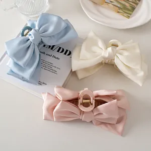 Close-up of satin ribbon bow hair claws in blue, white, and pink with glossy texture