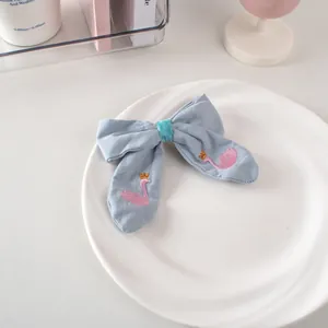 Dettaglio del fermaglio a fiocco azzurro con cigno rosa ricamato e corona dorata