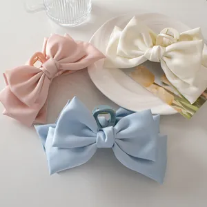 Detailed view of large satin bow hair claws in pink, cream, and blue colors