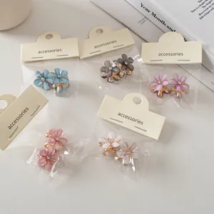 Dettaglio di mini mollette per capelli a fiore pastello con strass e base dorata