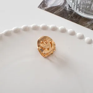 Close-up of a small golden metal smiley face hair claw clip on a white ceramic tray